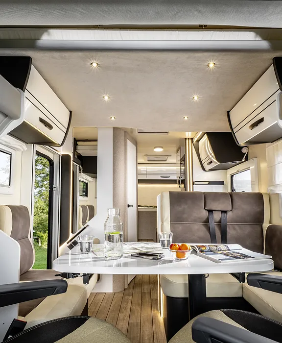 Wohnmobil steht unter einem Baum an einer felsigen Küste, mit Blick auf das Meer und Sonnenuntergangshimmel.