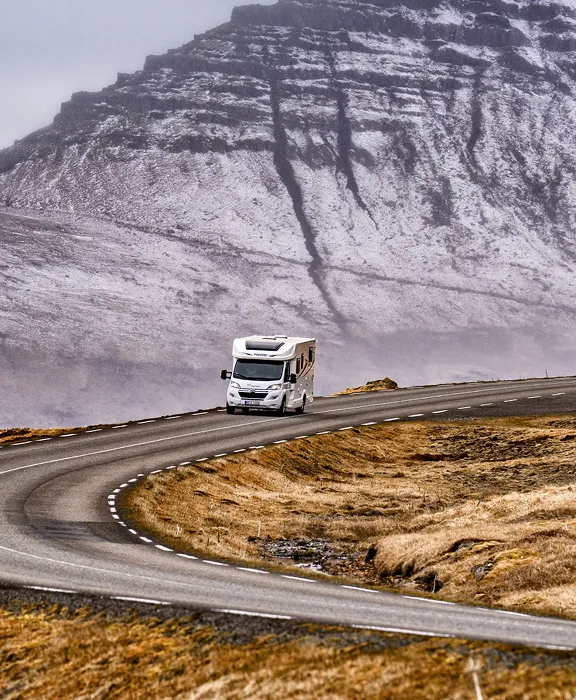 Wohnmobil fährt auf kurviger Straße vor schneebedecktem Bergmassiv.
